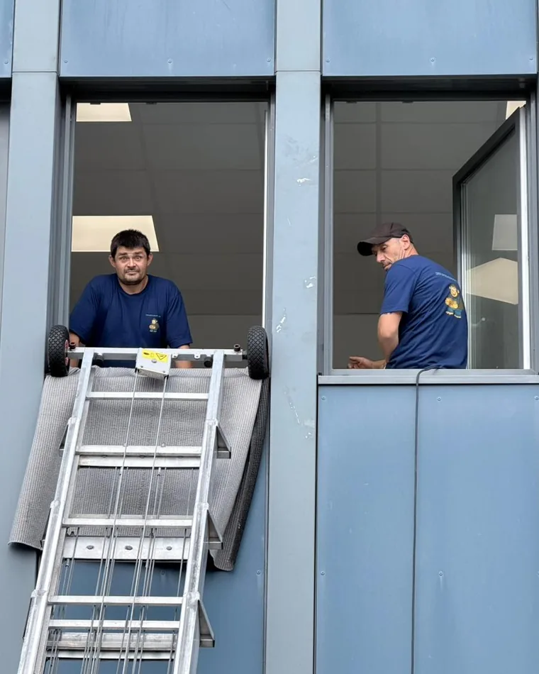 Zwei Mitarbeiter nehmen Umzugsgut am Fenster von der Schiene des Möbellifts ab